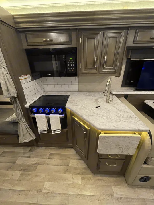 RV rental kitchen featuring a light grey countertop, dark cabinets, white subway tile backsplash, microwave, and stove.. Jayco Alante 29F 2023