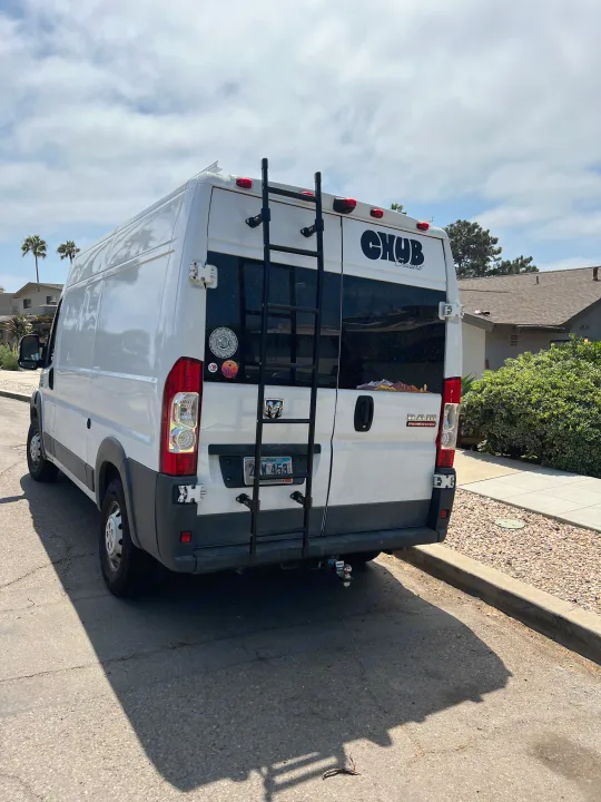 A white Ram ProMaster van, an ideal RV rental for your next road trip, parked on a sunny street with a rear ladder.. Dodge Ram Promaster 2500 2017