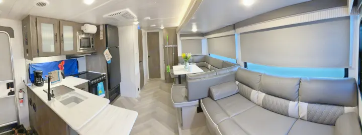 Bright RV rental interior: kitchen with coffee maker & stove, leading to U-shaped dinette & lounge area, gray modern design.. Forest River Wildwood X-Lite 2022
