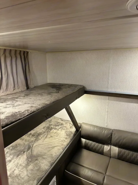 Inside an RV rental: a modern bunk bed setup and a sleek gray sofa offer comfortable sleeping and living space.. Forest River Wildwood X-Lite 2022