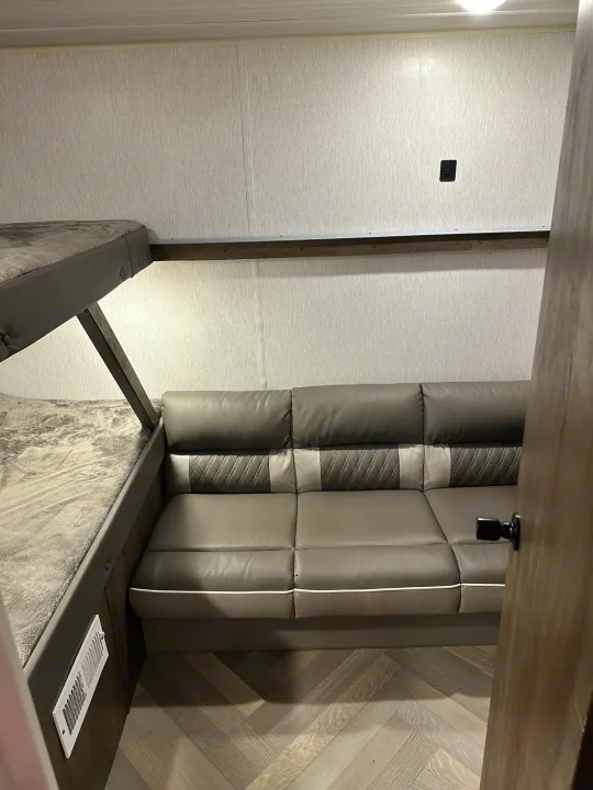 Cozy RV rental interior: grey bunk beds and comfortable sofa on herringbone floor. Perfect for travel.. Forest River Wildwood X-Lite 2022