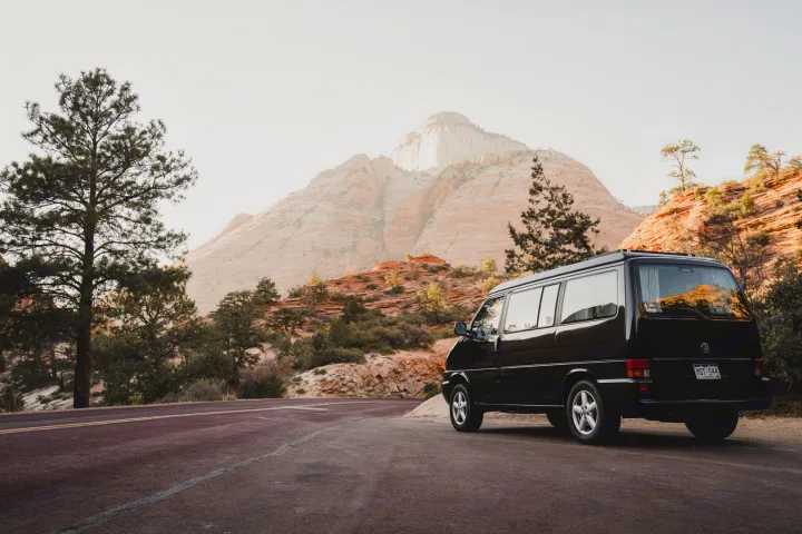 Black RV rental parked on a winding road, with majestic, light-colored mountains in the distance.. Volkswagen Eurovan MV 2002