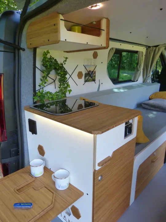 Cozy RV rental interior with a built-in kitchen, bed, and stylish storage solutions.. Renault Trafic aménagé avec kit North West de VAN MANIA 2024