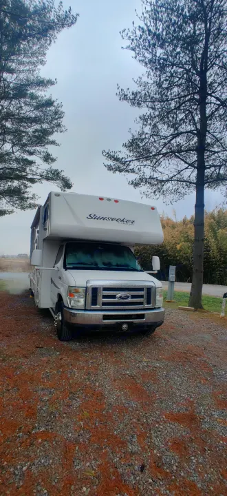 White Sunseeker RV rental motorhome parked on gravel campsite with trees, ideal for outdoor travel adventures.. Forest River Sunseeker 2012