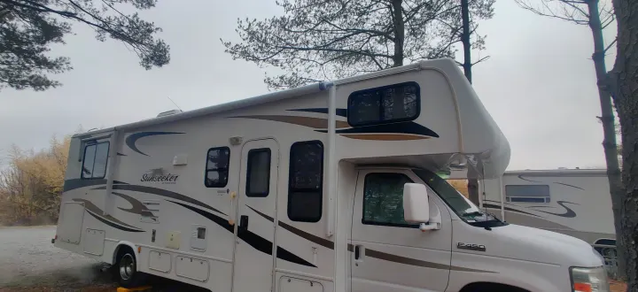 White Class C Sunseeker RV rental with brown decals, parked at a wooded campsite on an E-450 chassis.. Forest River Sunseeker 2012