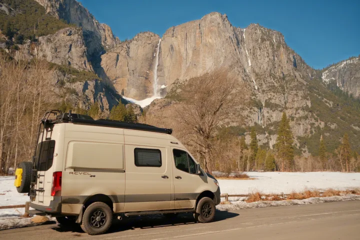 Exploring Yosemite with an RV rental: a white camper van facing a grand waterfall & snowy mountains.. Other Revel 2023