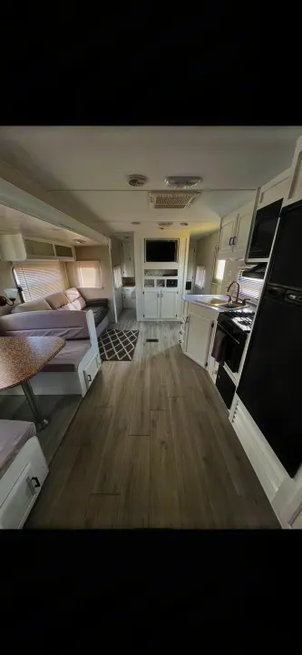 Modern and spacious RV rental interior with light wood flooring, a full kitchen, dinette, and living area with a TV.. Coachmen Catalina 2012