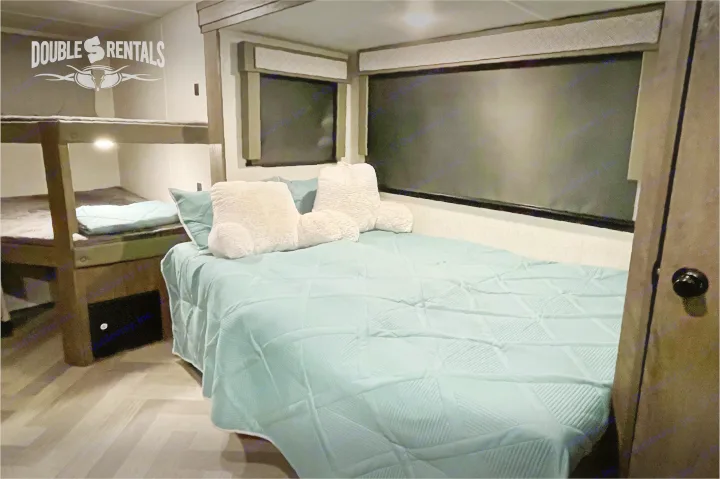Cozy RV rental interior featuring a main bed with plush pillows and comfortable bunk beds for a family adventure.. Forest River Wildwood X-Lite 2020