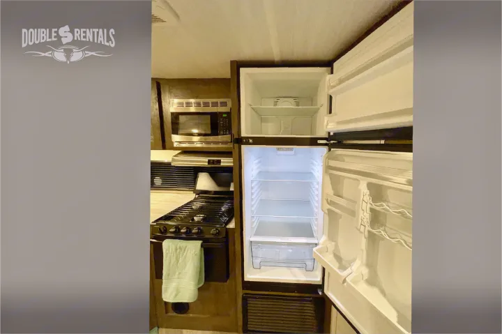 Explore this clean RV rental kitchen featuring an open, empty fridge/freezer, microwave, and gas stove.. Forest River Wildwood X-Lite 2020