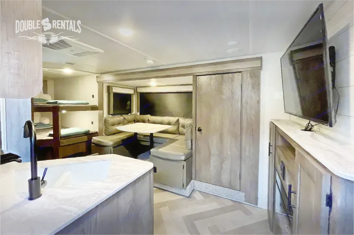 Modern rv rental interior: view from kitchen with sink towards bunk beds, dining area with table, and TV entertainment center.. Forest River Wildwood X-Lite 2020