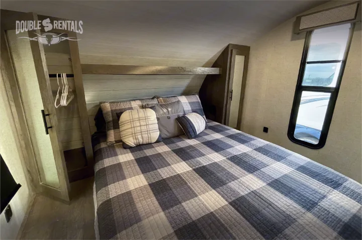 Inside a cozy RV rental bedroom featuring plaid bedding, a window, and built-in storage. Ideal for travelers.. Forest River Wildwood X-Lite 2020