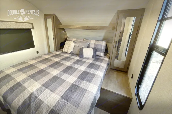 Cozy RV rental bedroom with comfortable plaid bed, overhead storage, and natural light from windows. Ideal for road trips.. Forest River Wildwood X-Lite 2020
