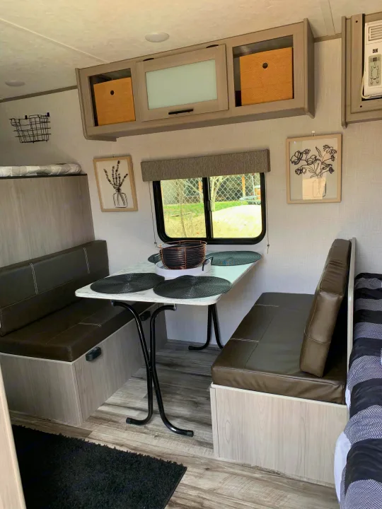 Cozy RV rental dinette setup with table, comfy benches, overhead cabinets, and window view for travel.. Dutchmen Coleman Lantern LT 2023