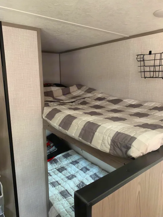 Inside an RV rental: two comfy bunk beds with gray and white checkered quilts, ideal for compact travel adventures.. Dutchmen Coleman Lantern LT 2023