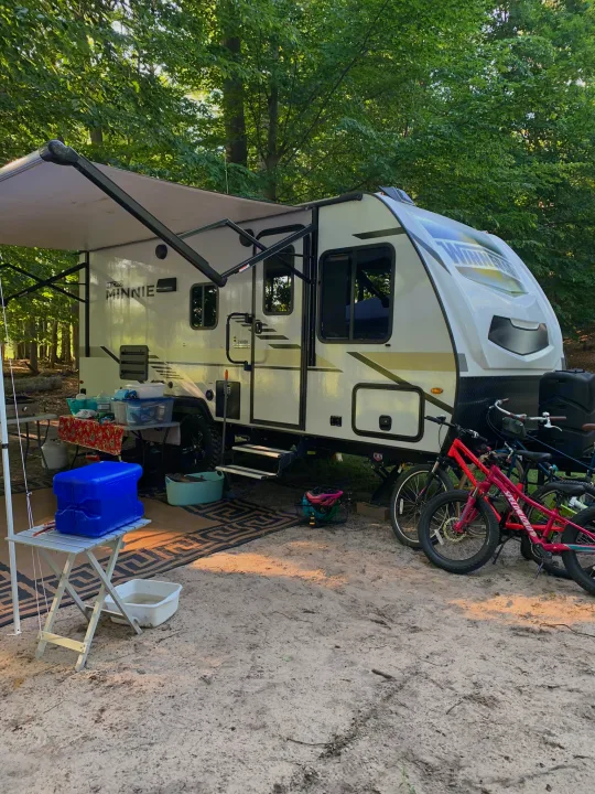 Campsite scene featuring a parked Winnebago Micro Minnie RV rental, with an awning out, camping gear, and bikes ready for adventure.. Winnebago Micro Minnie 2021