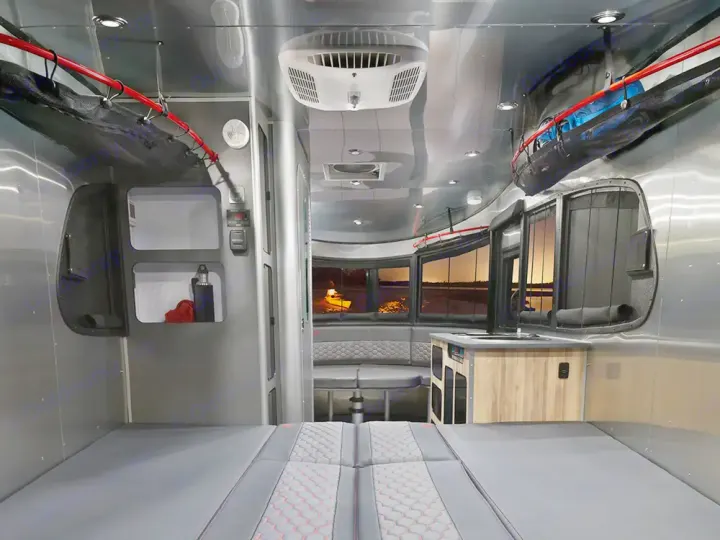Spacious RV rental interior featuring a comfortable bed, dinette, kitchen, and large scenic windows. Ideal for travel adventures.. Airstream Basecamp 2022