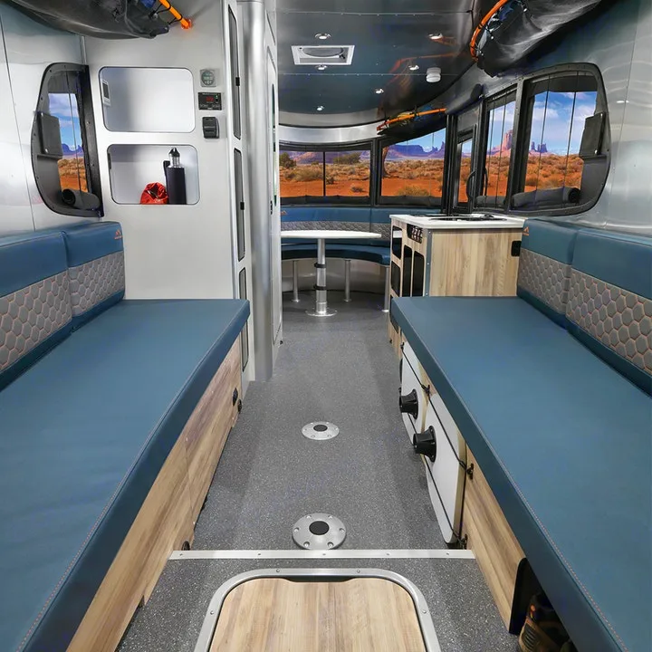 Spacious RV rental interior with blue cushioned seating, wood-look cabinetry, and panoramic desert views.. Airstream Basecamp 2022