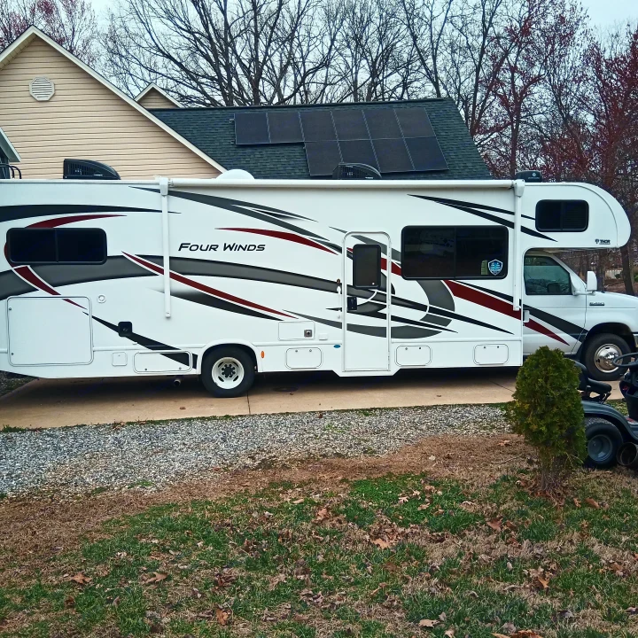 A white Four Winds RV is parked on a concrete pad next to a house with solar panels on its roof. Consider this RV rental!. Thor Four Winds 2022