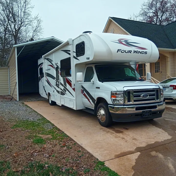 White Ford Four Winds RV rental parked on a concrete driveway with a metal carport and house in the background.. Thor Four Winds 2022