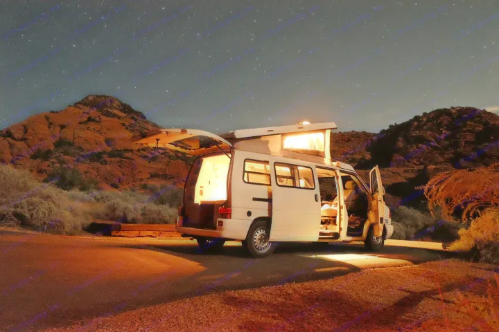 Experience starry nights in an RV rental. A white camper van, lit within, with open doors, parked under a vast starry sky.. Volkswagen Eurovan Full Camper 2000