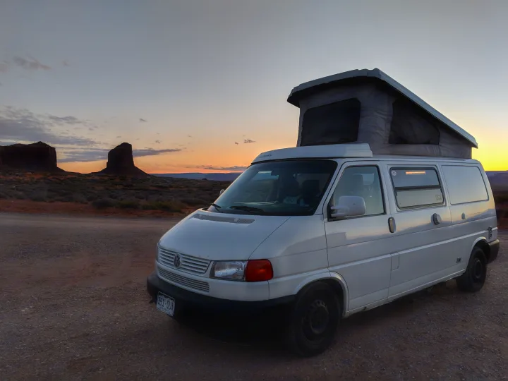 An RV rental - a white pop-top camper van - parked on a dirt road, silhouetted by desert buttes at a beautiful sunset.. Volkswagen Eurovan Full Camper 2000