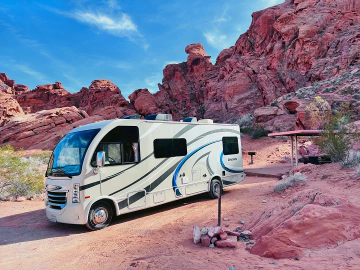 An RV rental is parked at a desert campsite with stunning red rock formations under a blue sky.. Thor Vegas 2017