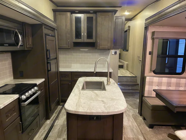 Modern RV rental interior: well-equipped kitchen with island, stove, and cozy dinette. Comfort on the road awaits.. Grand Design Reflection 2021