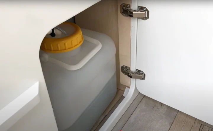 RV rental: Interior view of a white cabinet with an open door, revealing a large translucent water tank with a yellow cap and metal hinges.. volkswagen Caddy 2010