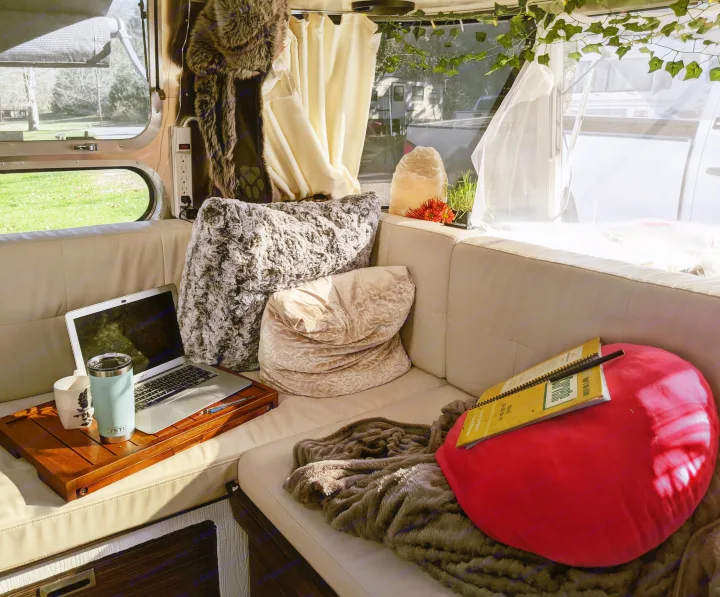 Cozy RV rental interior featuring a laptop on a wooden tray, plush pillows, and outdoor views from the window.. Airstream International 2015