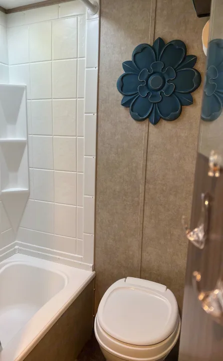 Compact RV rental bathroom with white shower/tub, toilet, and a decorative blue flower on the tan wall.. Coachmen Clipper 2016