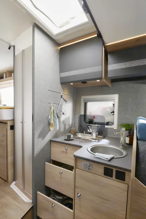 Compact RV rental interior featuring a modern kitchen with sink, stove, and ample storage, plus a shower. Ideal for travel.. Dethleffs JUST T7052 DBM 2023
