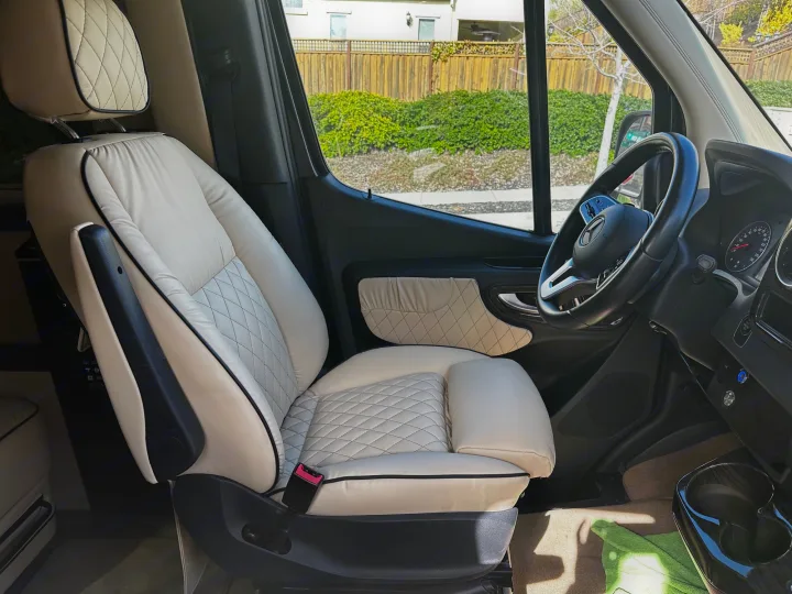 Bright RV rental interior showcases a luxurious cream quilted leather passenger seat with black piping and a Mercedes-Benz steering wheel.. Ultimate Toys Ultimate Cruiser 2021