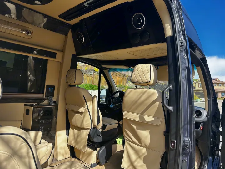 Spacious luxury RV rental van interior, featuring custom tan leather seating, wood trim, and an entertainment system.. Ultimate Toys Ultimate Cruiser 2021