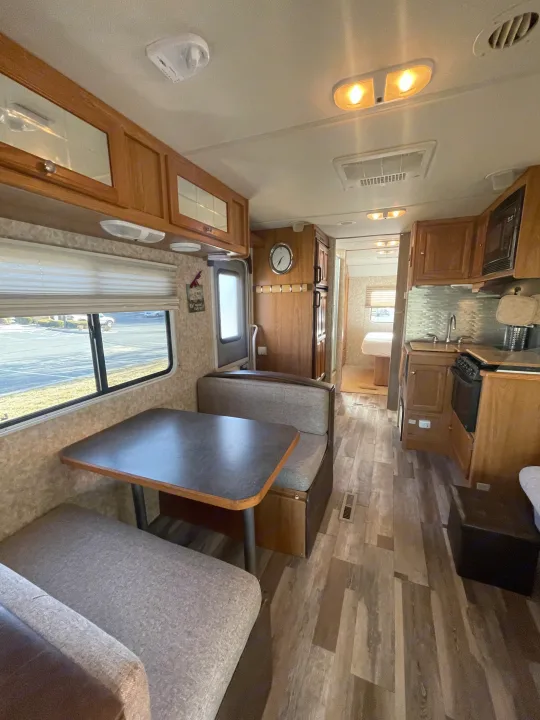 Inside an RV rental: full view of the dinette, well-equipped kitchen, and cozy bedroom beyond, with light wood accents.. Safari Ivory 2006