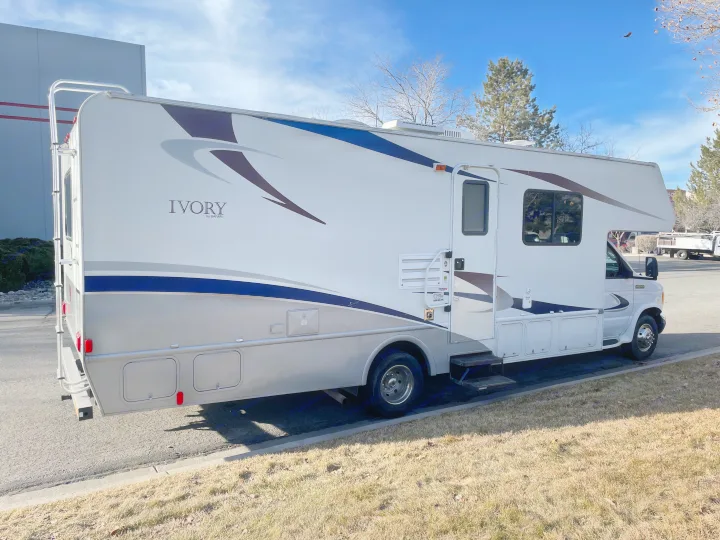 A white Ivory by Safari Class C RV rental with blue accents is parked outdoors on a sunny day.. Safari Ivory 2006