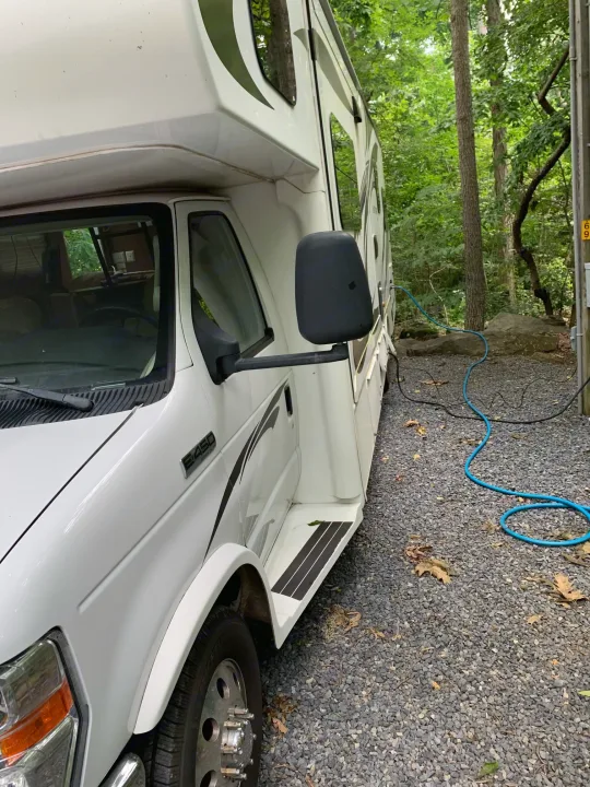 White RV rental parked on gravel campsite, hooked up amidst green trees.. Jayco Greyhawk 2014