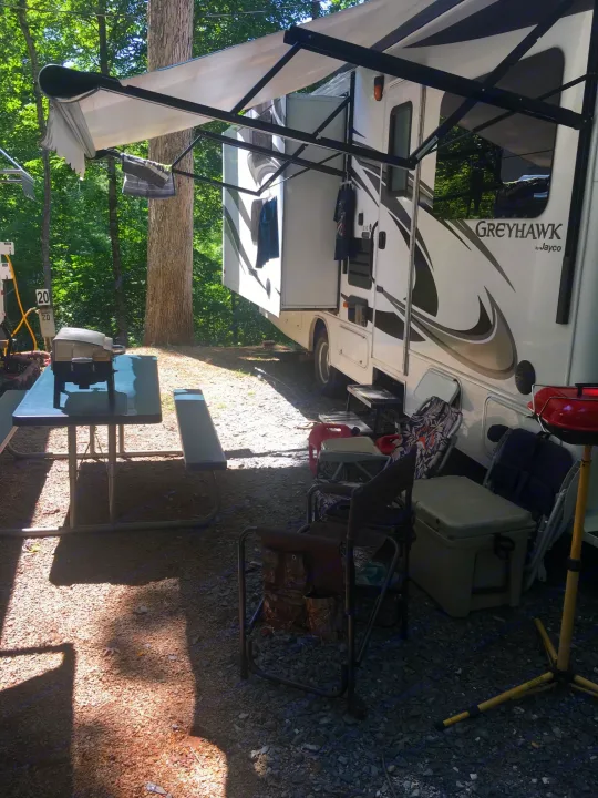 This RV rental is set up at a shaded campsite with an extended awning, picnic table, and chairs.. Jayco Greyhawk 2014