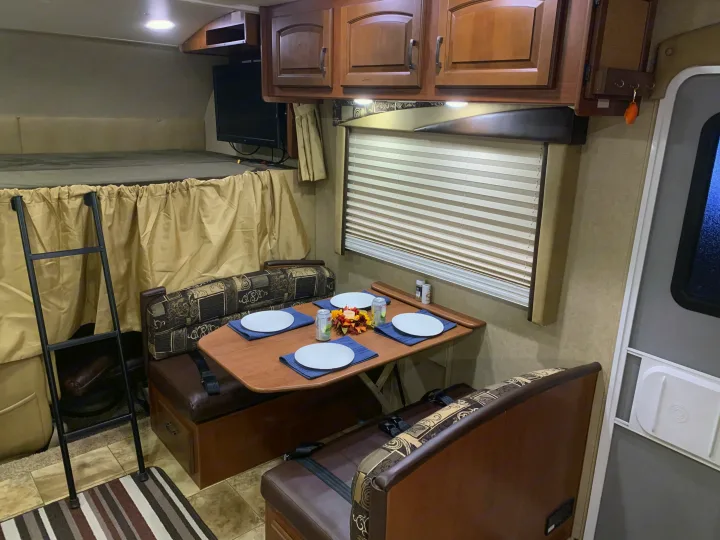 Cozy RV rental interior with a furnished dinette, overhead cabinets, a mounted TV, and an upper sleeping bunk with a ladder.. Jayco Greyhawk 2014
