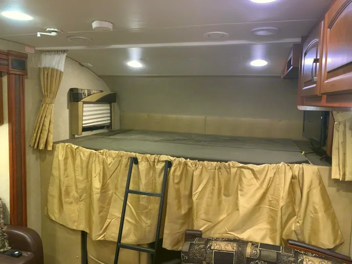 Cozy RV rental sleeping area featuring an overhead bunk bed with a ladder, privacy curtain, and bright interior lighting.. Jayco Greyhawk 2014