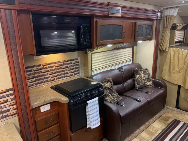 RV rental interior: full kitchen with microwave, stove, and comfortable brown leather couch with bunk beds.. Jayco Greyhawk 2014