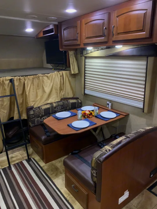 View of a modern rv rental interior, showing a dinette with place settings, a bunk bed with ladder, and ample storage.. Jayco Greyhawk 2014