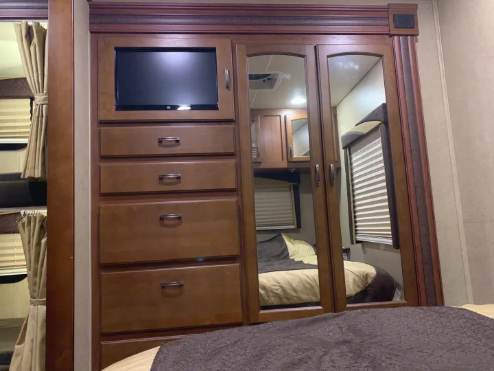 RV rental bedroom features: built-in TV, dresser drawers, and mirrored closets reflecting the bed and blinds.. Jayco Greyhawk 2014
