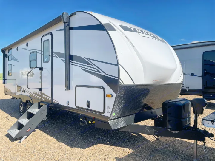 A sleek white Tracer travel trailer, perfect for your next RV rental adventure, shown with an extended awning and deployed steps on a gravel lot.. Forest River Tracer 2022