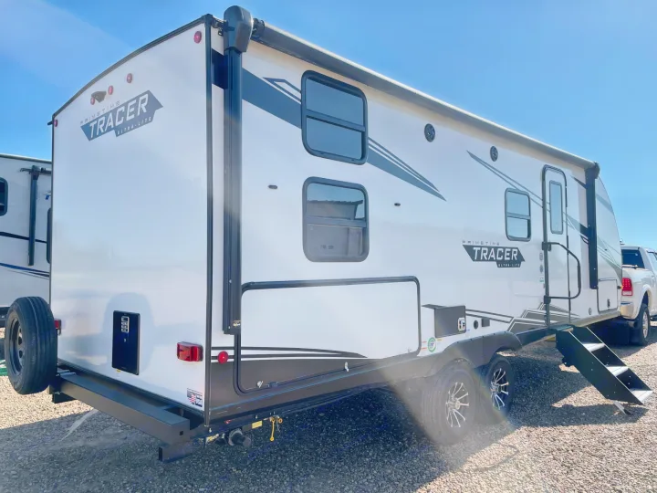 A white Primetime Tracer Ultra-Lite travel trailer, featuring an awning, windows, and entry steps, an ideal RV rental option.. Forest River Tracer 2022