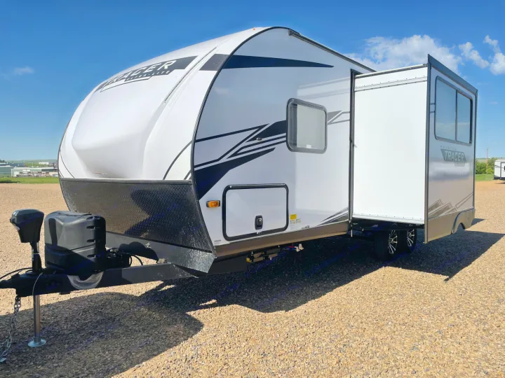 This white travel trailer, ideal for RV rental, features an extended slide-out. Ready for outdoor adventures under a clear sky.. Forest River Tracer 2022