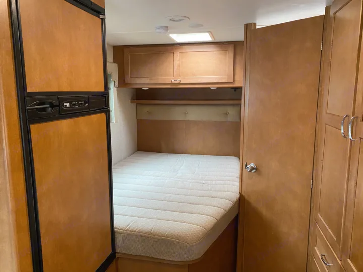Inside this RV rental: a compact bedroom with a mattress, overhead cabinets, and a refrigerator on the left.. Winnebago Minnie Winnie 2017