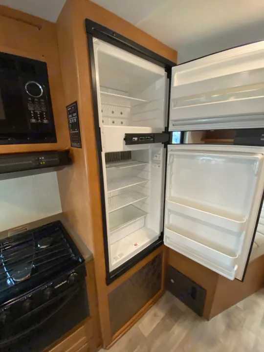 RV rental kitchen: An open refrigerator revealing shelves, alongside a microwave and stove, for convenient living on the go.. Winnebago Minnie Winnie 2017