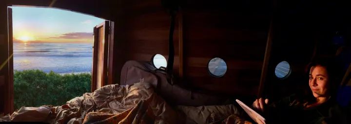 Cozy RV rental: Woman on a bed with an expansive ocean sunset view, guitar case, and portholes in a wooden interior.. Custom Camper 2017