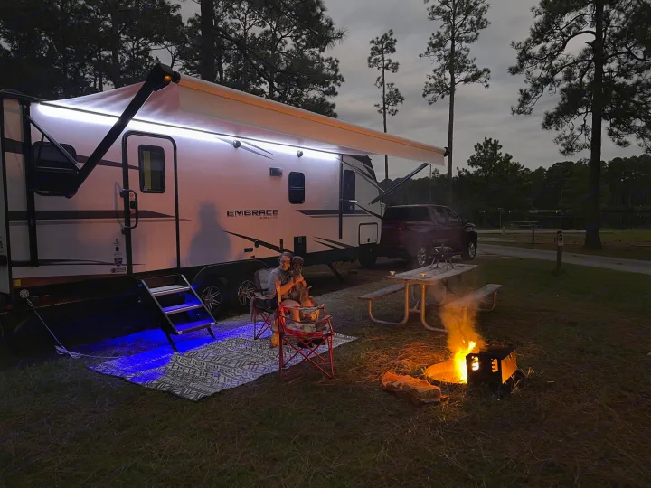 Cozy RV rental camping evening: a person and dog by the fire pit, illuminated camper, and picnic table.. Cruiser RV Embrace Ultra Lite 2022