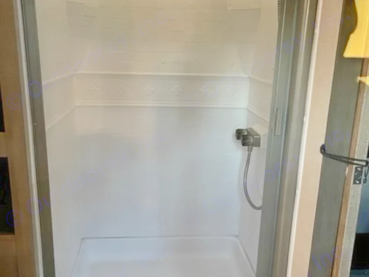 Compact, bright white shower stall inside an RV rental, featuring a handheld showerhead. Ideal for road trip travelers.. Grand Design Imagine 2022